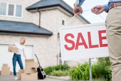 Realtor putting up a sale sign on the lawn of a house.